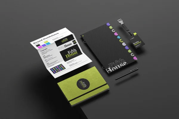 Branding materials including a black notebook with colorful circular icons, a yellow notebook with a black elastic band, a black name badge reading 'Kashia Spalding,' a pen, and a printed brand guidelines document with various logo designs for 'Fifth House' on a gray surface.