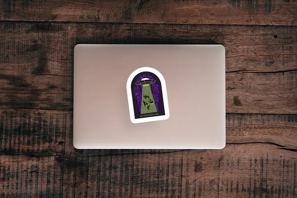 Aconundrum sticker on a laptop lid resting on dark wood, showing an arched doorway with a figure in silhouette.