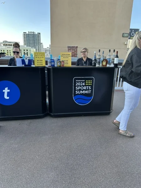 Registration counter with a black Ticketmaster-branded front panel carrying the Sports Summit badge, staff working behind it.